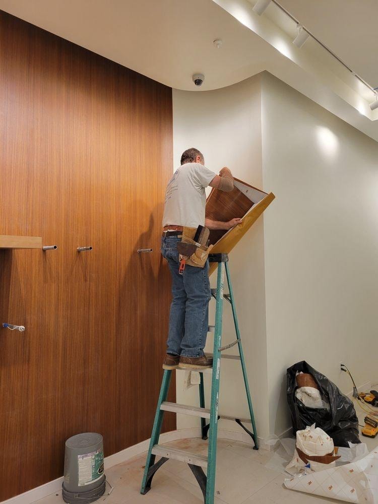 Scott on ladder installing wood wall panels in commercial space